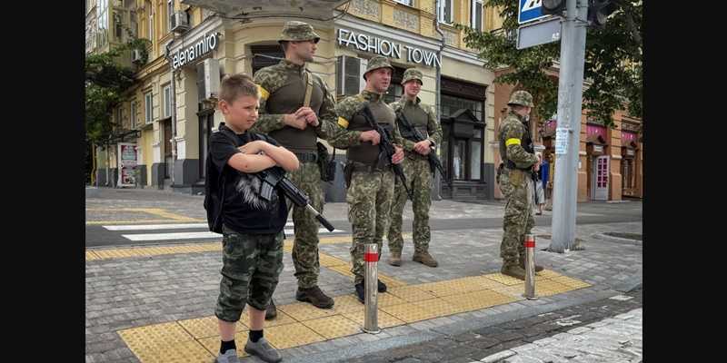 Seorang anak laki-laki dengan senapan mainan berdiri di sebelah pejuang Ukraina di Kyiv/Foto RFE